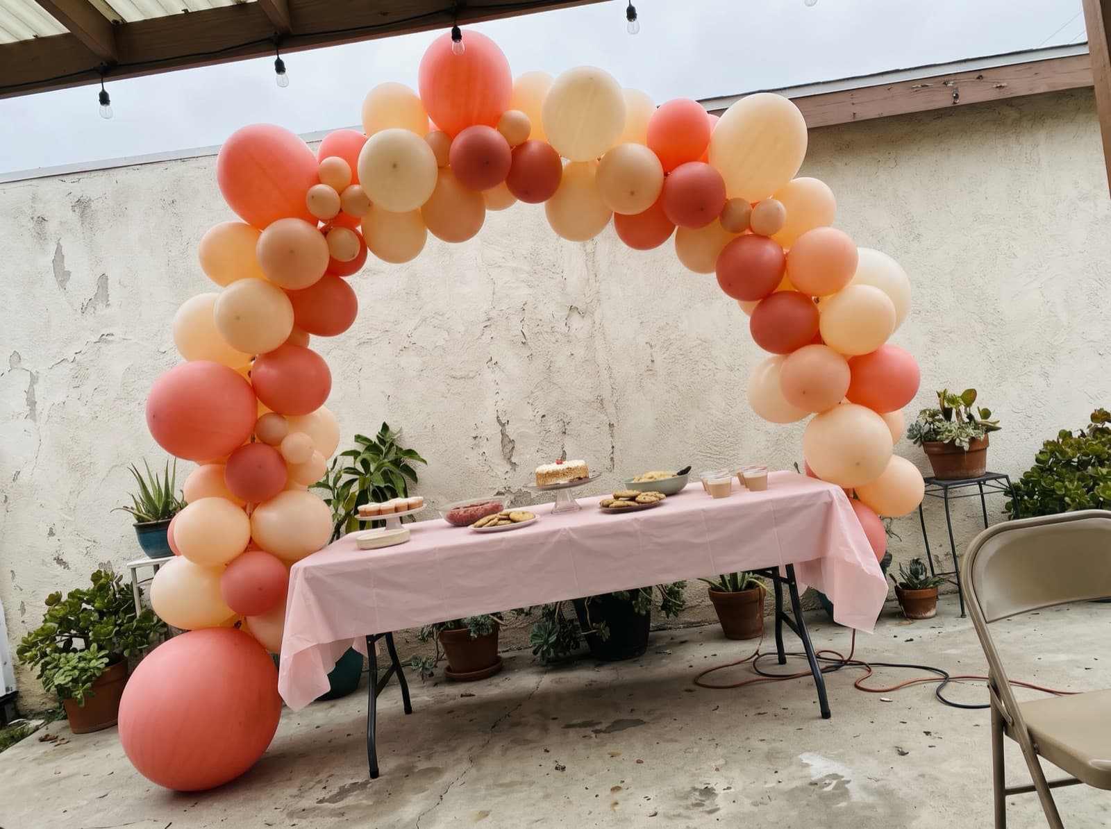 Organic balloon arch in coral, peach and cream over a dessert table on a San Diego backyard patio